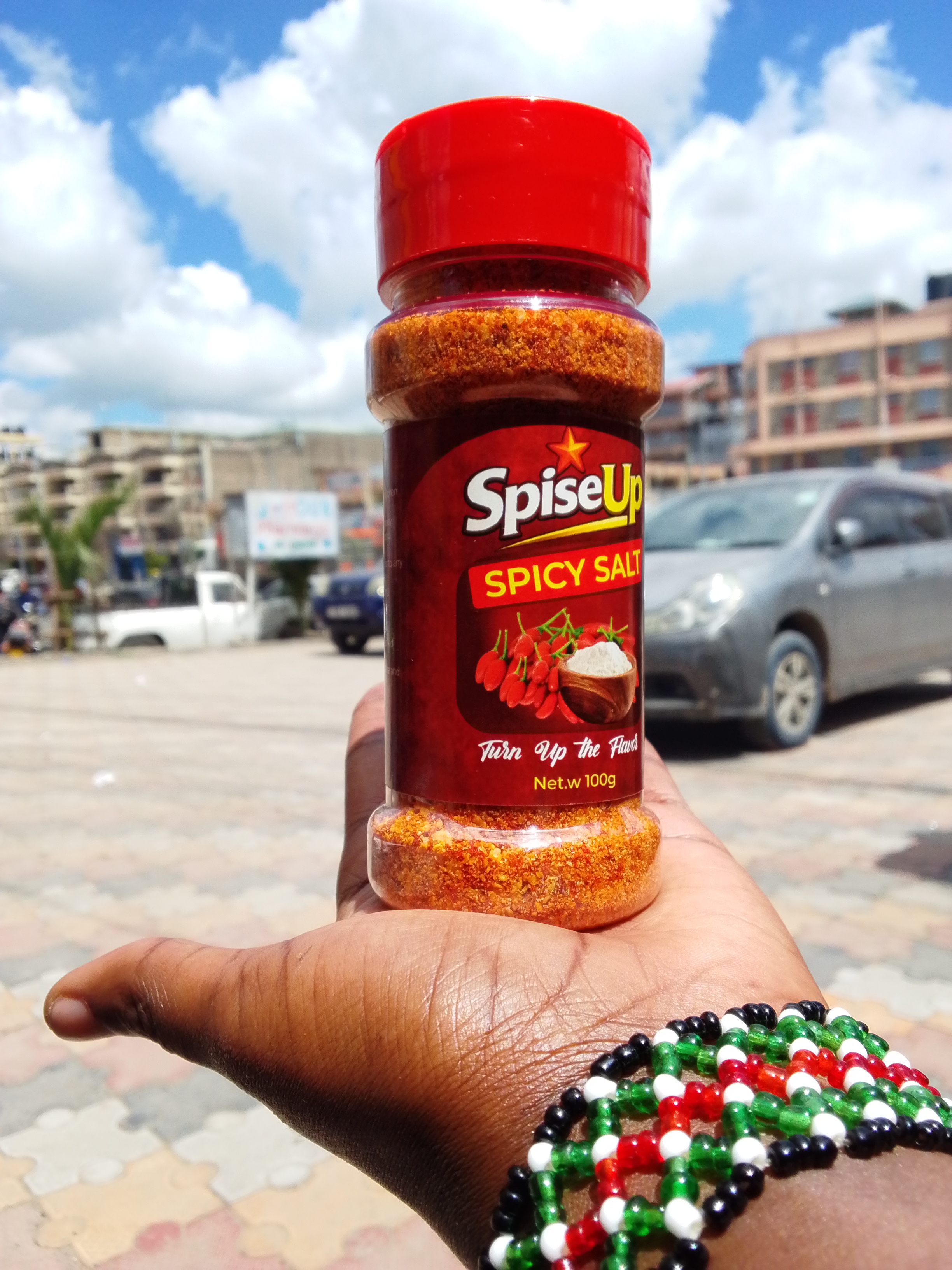 A hand holding a SpiseUp Spicy Mix bottle out on the streets of Kitengela